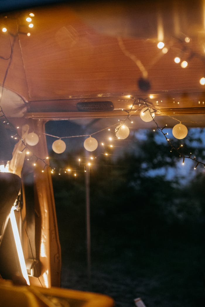 A warmly lit camper van interior, adorned with string lights, creating a cozy ambiance.